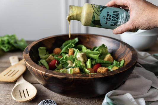 Hand pouring Caesar dressing into a bowl with salad