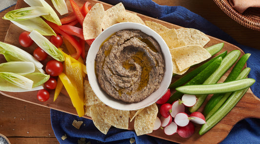 Small serving bowl of Black Bean Hummus with assorted vegetables and chips arranged on the wooden platter