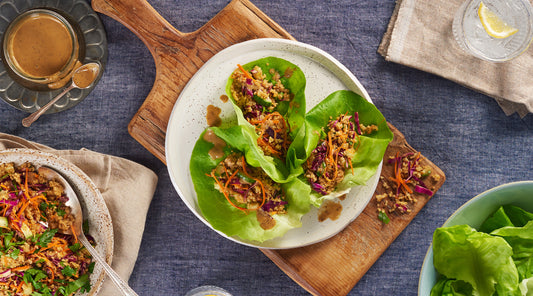Plate with three Veggie Bulgur Lettuce Wraps served on a cutting board, with a bowl of lettuce and a bowl of filling nearby.