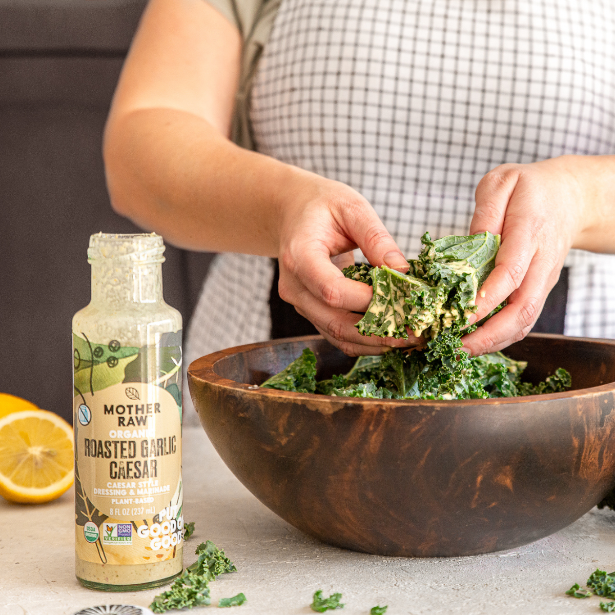 Roasted Garlic Caesar Dressing Bottle with women mixing kale in a salad bowl